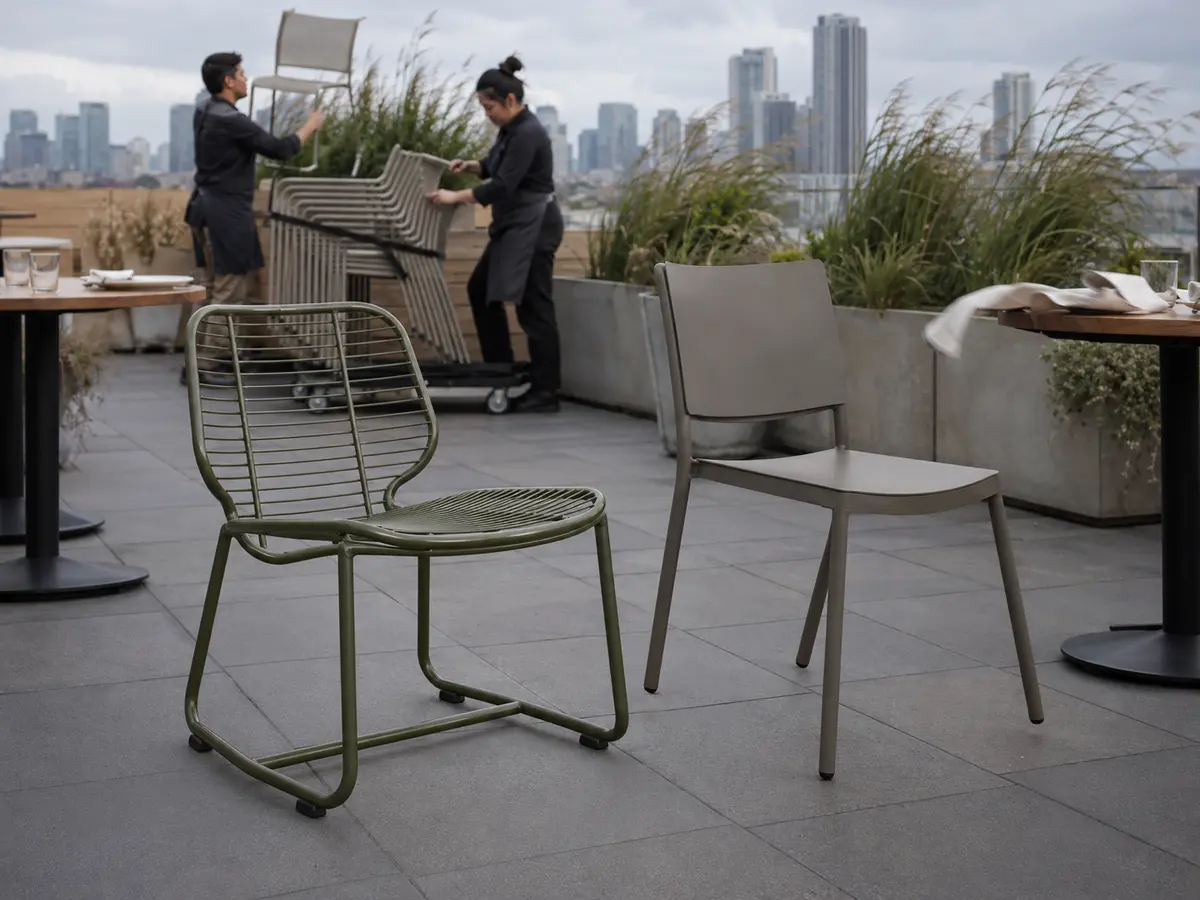Open-back and solid-back chairs on a breezy rooftop while staff secure patio furniture